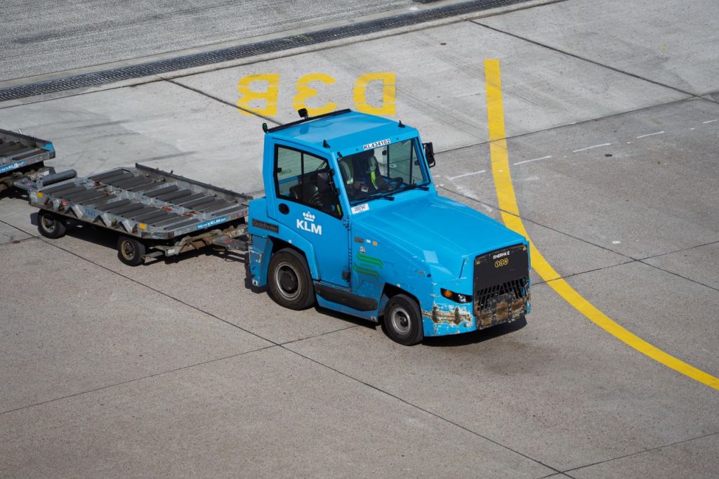 KLM Ground Support Equipment towing baggage carts on airport tarmac.